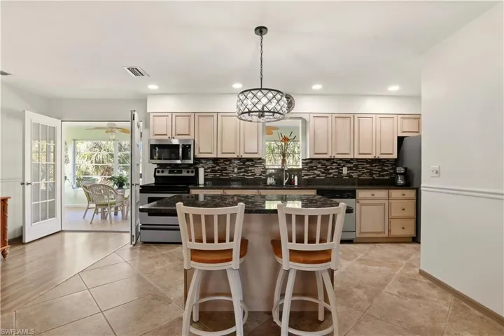 Kitchen featuring stainless steel appliances, a kitchen island, a kitchen breakfast bar, decorative light fixtures, and tasteful backsplash