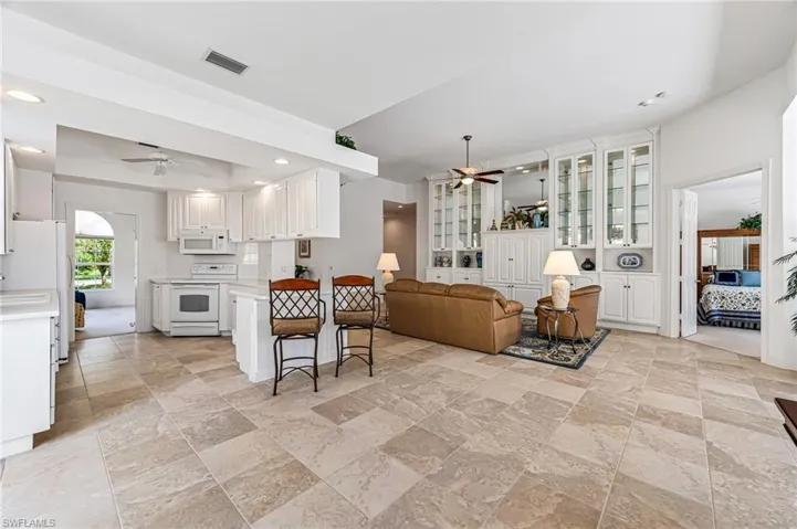 Kitchen featuring ceiling fan, white appliances, light tile floors, a breakfast bar, and white cabinets
