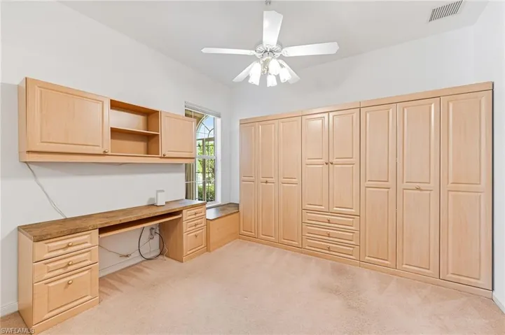 Unfurnished office featuring built in desk, ceiling fan, and light colored carpet