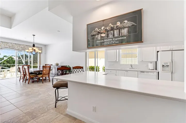 Kitchen with an inviting chandelier, white appliances, white cabinets, pendant lighting, and sink