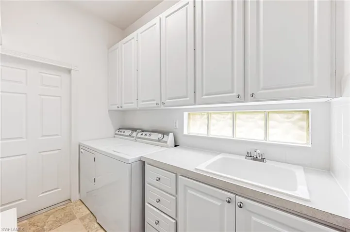 Clothes washing area featuring cabinets, sink, light tile flooring, and washing machine and clothes dryer