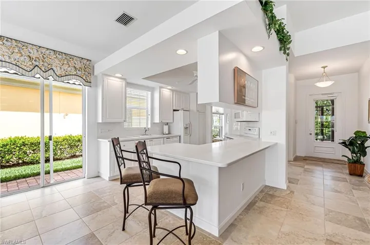 Kitchen with white refrigerator with ice dispenser, kitchen peninsula, light tile floors, hanging light fixtures, and white cabinets
