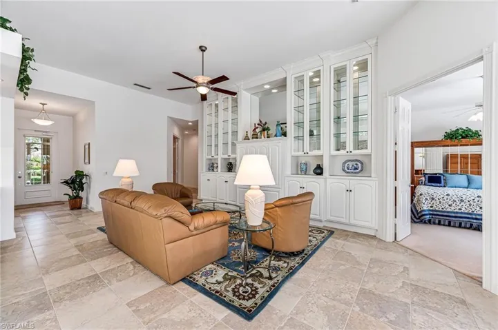Living room with light colored carpet, built in shelves, and ceiling fan