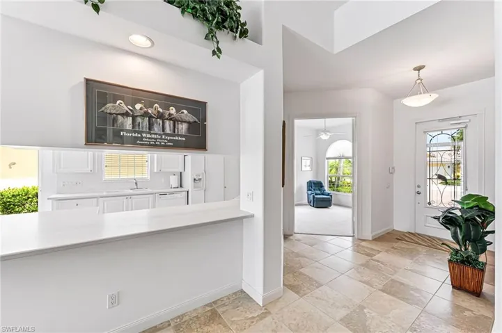 Kitchen with decorative light fixtures, white cabinets, light tile flooring, and plenty of natural light