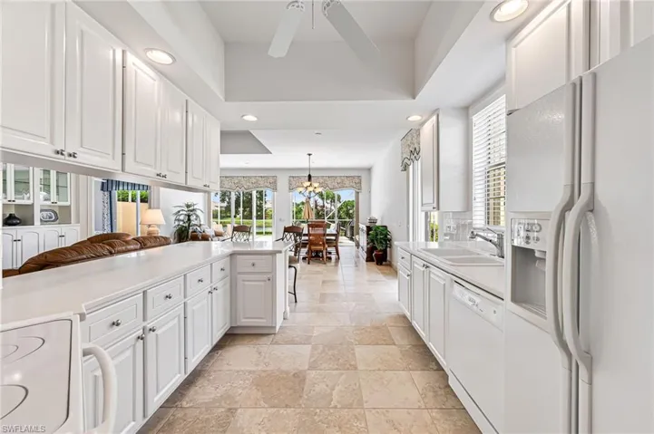 Kitchen with a tray ceiling, white appliances, light tile floors, sink, and white cabinets