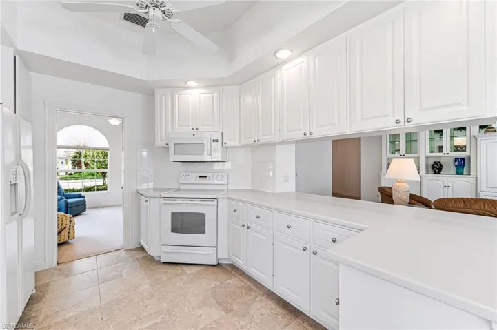 Kitchen with white cabinets, ceiling fan, white appliances, and light tile floors