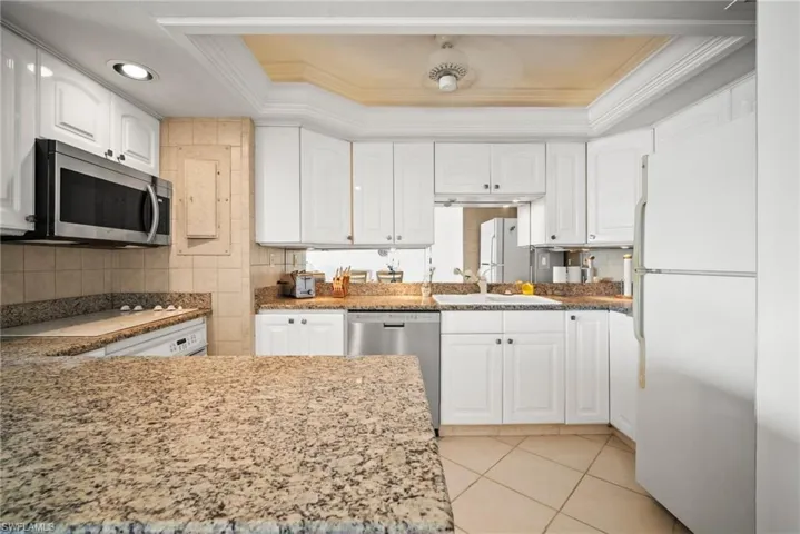 Kitchen featuring stainless steel appliances, ornamental molding, a raised ceiling, and white cabinetry