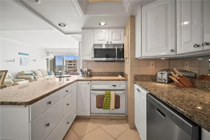 Kitchen with stainless steel appliances, crown molding, a peninsula, white cabinetry, and decorative backsplash