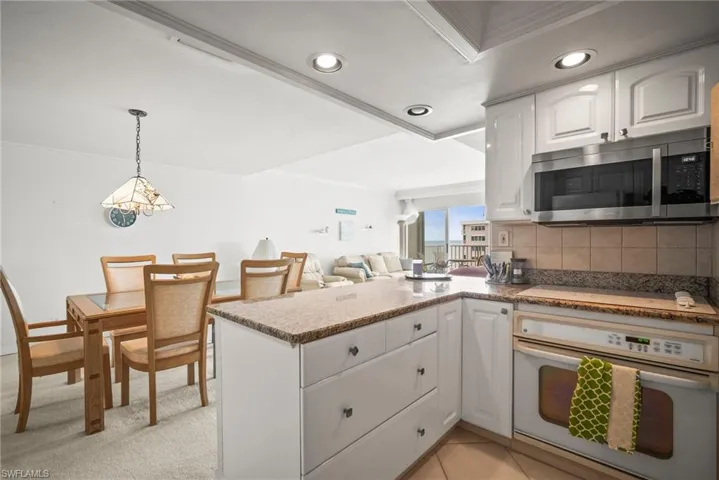 Kitchen featuring oven, stainless steel microwave, a peninsula, ornamental molding, and white cabinets