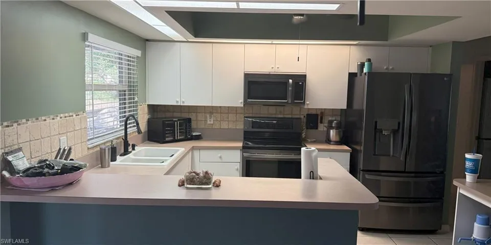 Kitchen featuring black fridge, stainless steel electric range, a sink, a peninsula, and light countertops