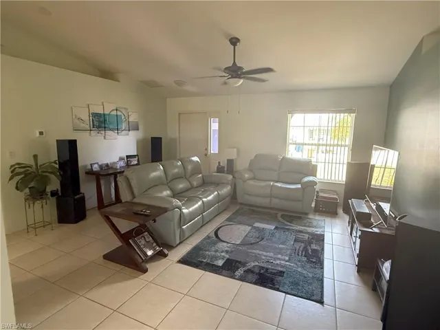 Living room with light tile patterned floors, ceiling fan, and lofted ceiling