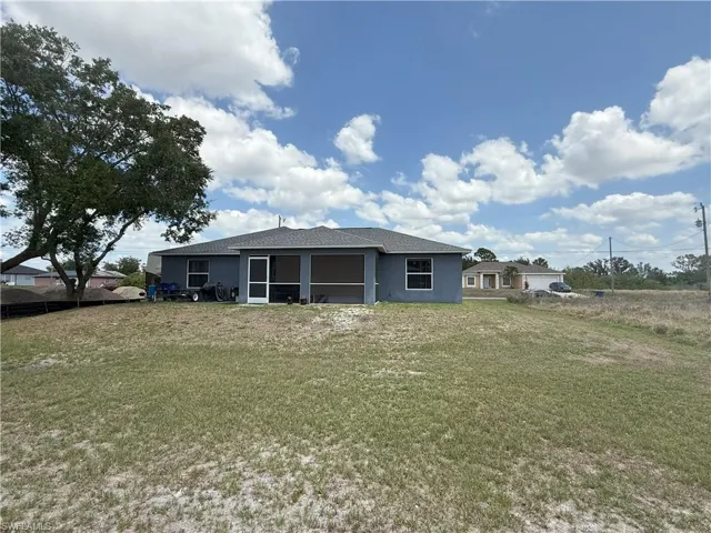Rear view of house featuring a sunroom, a lawn, and stucco siding