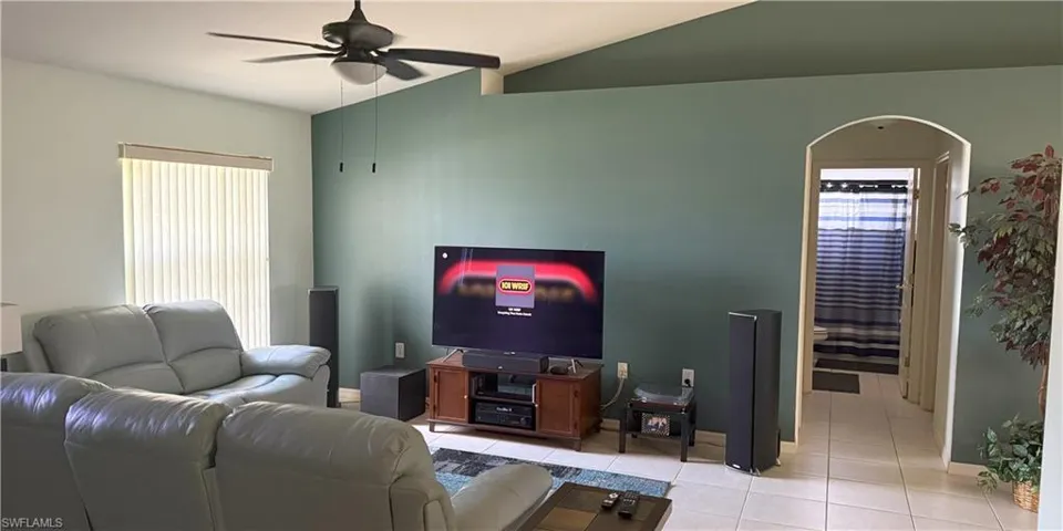 Living room with ceiling fan, light tile patterned flooring, lofted ceiling, baseboards, and arched walkways
