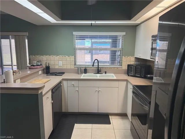 Kitchen featuring black appliances, a sink, light countertops, a peninsula, and decorative backsplash