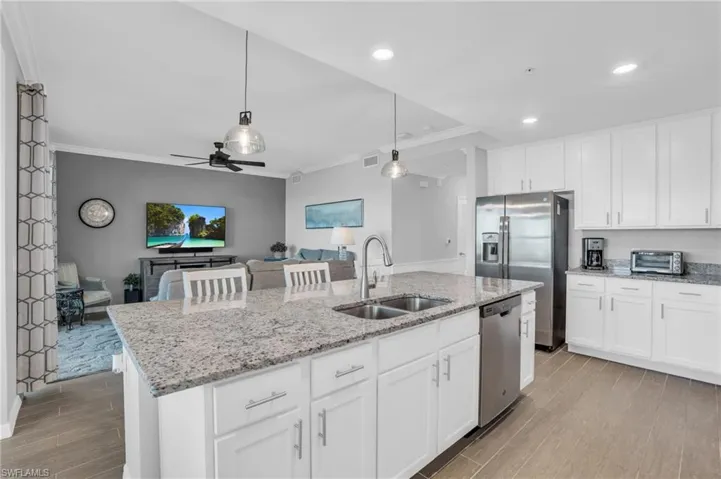 Kitchen with hanging light fixtures, stainless steel appliances, a kitchen island with sink, and ceiling fan