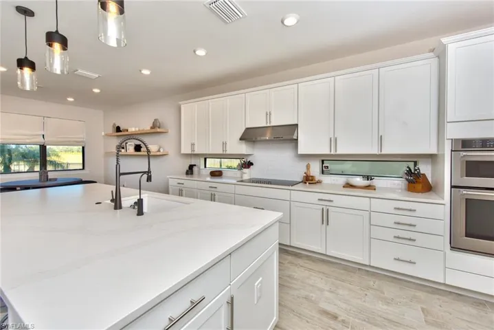 Kitchen with white cabinetry, open shelves, light wood-style floors, stainless steel double oven, and recessed lighting