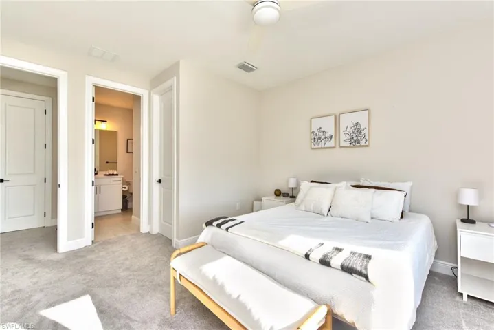 Bedroom featuring light colored carpet, a ceiling fan, and ensuite bath
