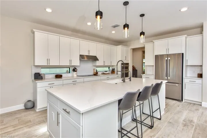 Kitchen featuring high quality fridge, light wood finished floors, hanging light fixtures, backsplash, and white cabinets
