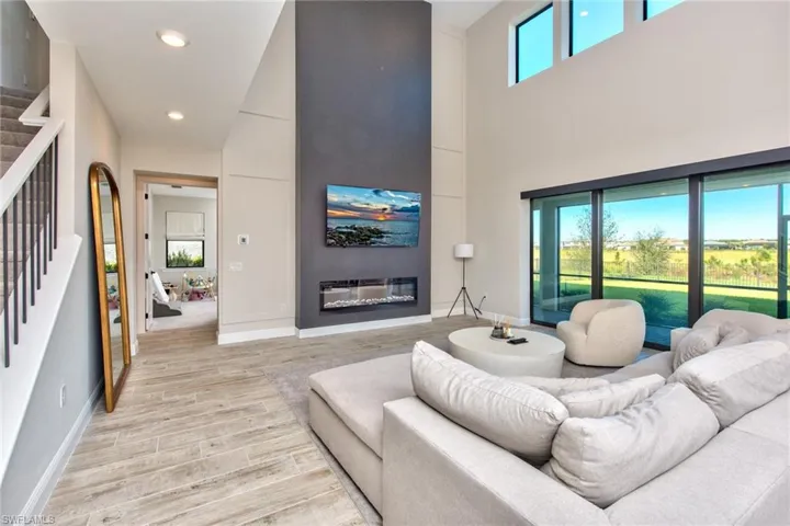 Living room with stairway, a glass covered fireplace, wood finished floors, recessed lighting, and a towering ceiling