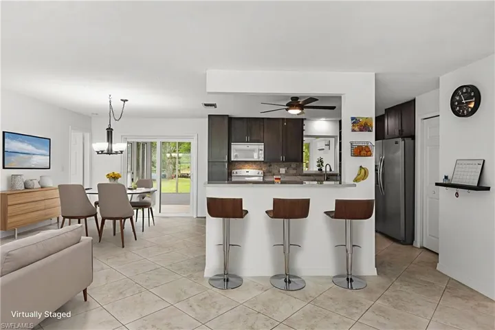Kitchen featuring white microwave, stainless steel fridge with ice dispenser, a kitchen breakfast bar, decorative backsplash, and a ceiling fan