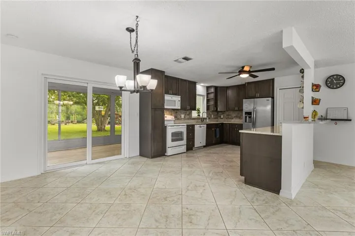 Kitchen featuring white appliances, dark brown cabinets, plenty of natural light, backsplash, and a textured ceiling