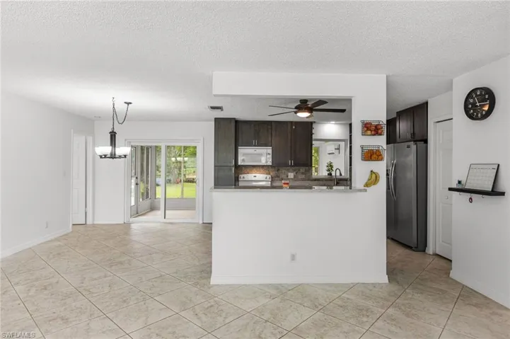 Kitchen featuring white microwave, stainless steel fridge, a chandelier, dark brown cabinets, and a ceiling fan