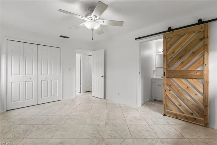 Unfurnished bedroom featuring a barn door, crown molding, ensuite bathroom, a ceiling fan, and a closet