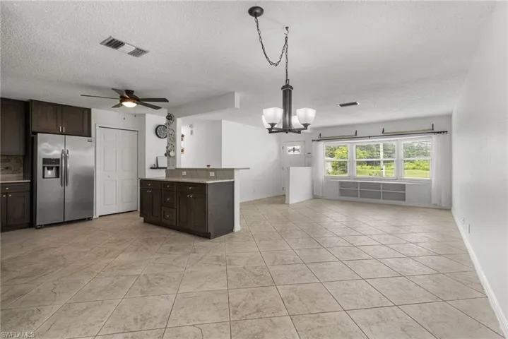Kitchen featuring stainless steel fridge with ice dispenser, a textured ceiling, a chandelier, open floor plan, and dark brown cabinets