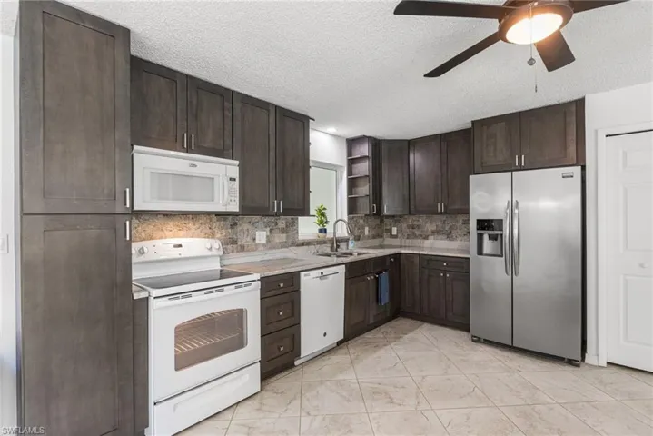 Kitchen with white appliances, open shelves, dark brown cabinets, a ceiling fan, and a textured ceiling