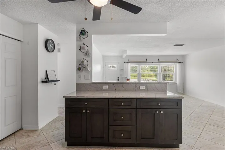 Kitchen featuring a textured ceiling, a ceiling fan, light tile patterned flooring, dark brown cabinets, and a peninsula