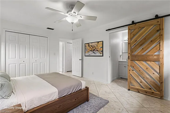 Bedroom with a barn door, crown molding, a closet, ensuite bath, and ceiling fan