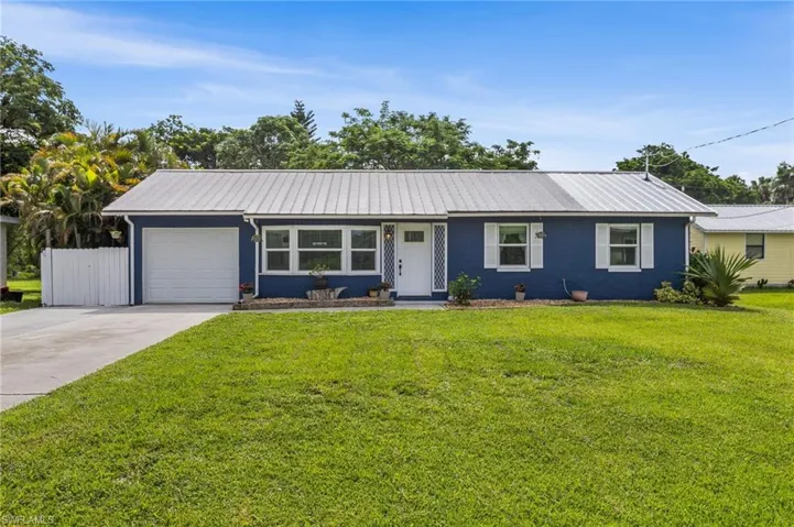 Single story home featuring an attached garage, a front yard, concrete driveway, and a metal roof