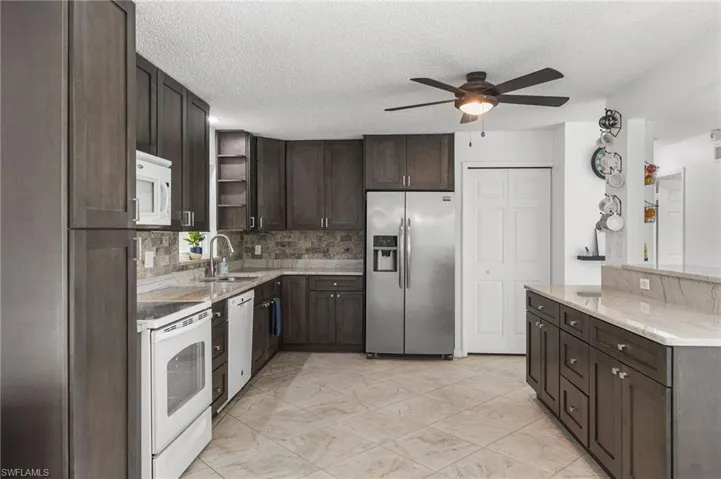 Kitchen with white appliances, a ceiling fan, open shelves, dark brown cabinetry, and backsplash
