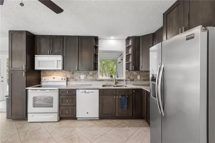 Kitchen with white appliances, open shelves, dark brown cabinetry, and a textured ceiling