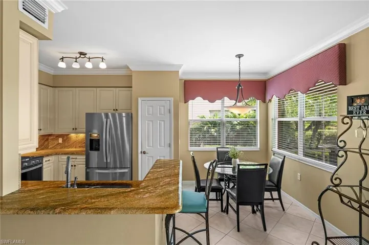 Kitchen featuring light tile patterned floors, hanging light fixtures, a peninsula, stainless steel fridge, and a kitchen bar