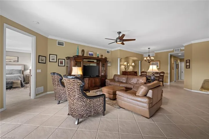 Living room with light tile patterned floors, a chandelier, crown molding, and ceiling fan
