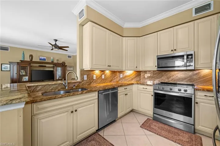 Kitchen with crown molding, appliances with stainless steel finishes, dark stone counters, and cream cabinetry