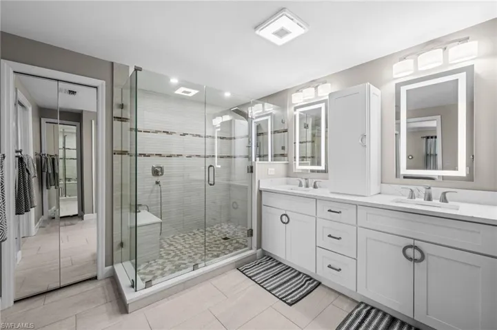 Full bathroom with double vanity, light tile patterned floors, and a stall shower