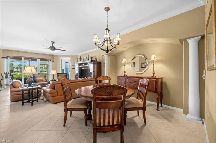 Dining room with decorative columns, light tile patterned floors, a chandelier, ornamental molding, and ceiling fan