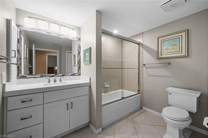 Bathroom featuring enclosed tub / shower combo, vanity, and light tile patterned flooring