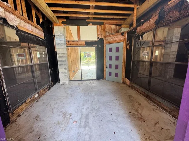 Exposed ceiling beams, concrete flooring, exterior sliding glass door, and an exterior door with window inserts