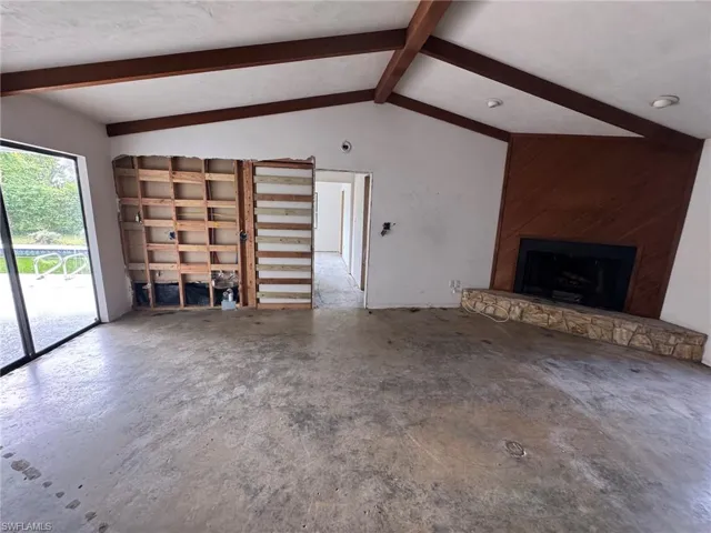 Vaulted ceiling with exposed wood beams, wood-paneled fireplace surround, stone hearth, and full-height glass panel
