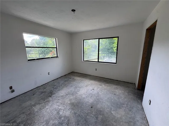 Unfinished interior space with two rectangular windows and an exposed concrete subfloor
