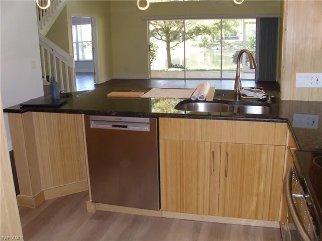 Kitchen featuring light wood finished floors, stainless steel appliances, dark stone countertops, and light wood finish cabinetry