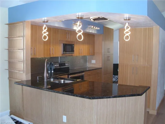 Kitchen featuring dark stone counters, pendant lighting, a peninsula, and stainless steel electric range