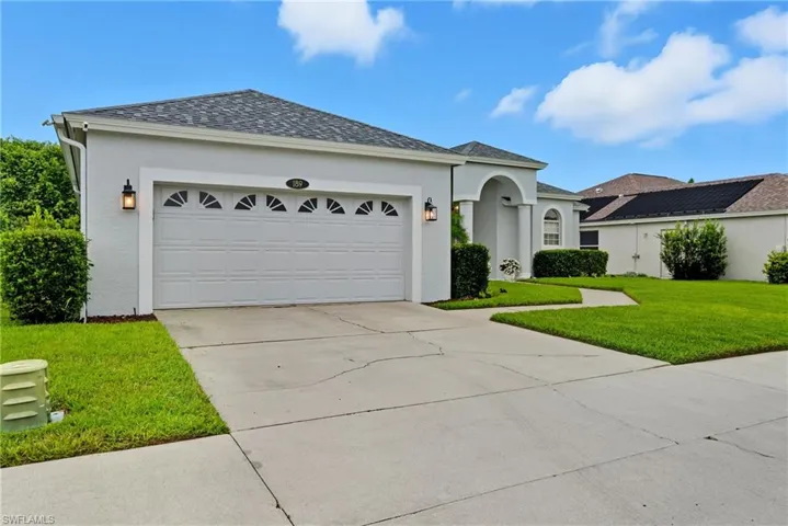 View of front of home with concrete driveway, roof with shingles, an attached garage, stucco siding, and a front lawn