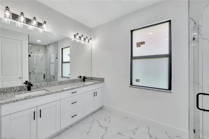 Bathroom featuring double vanity, marble look tiles, and a marble finish shower