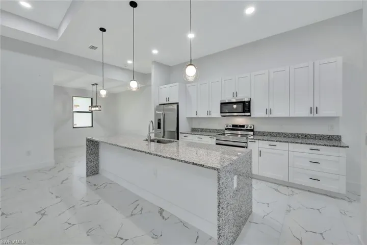 Kitchen featuring appliances with stainless steel finishes, white cabinetry, an island with sink, light stone counters, and recessed lighting