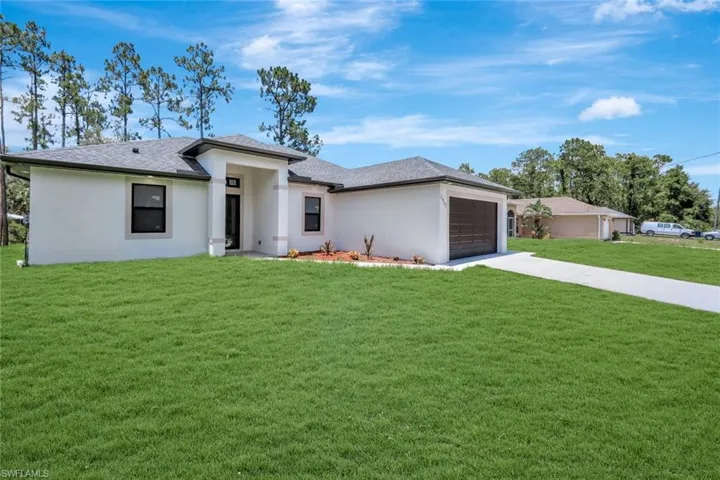 Prairie-style house featuring a front lawn, concrete driveway, an attached garage, stucco siding, and roof with shingles