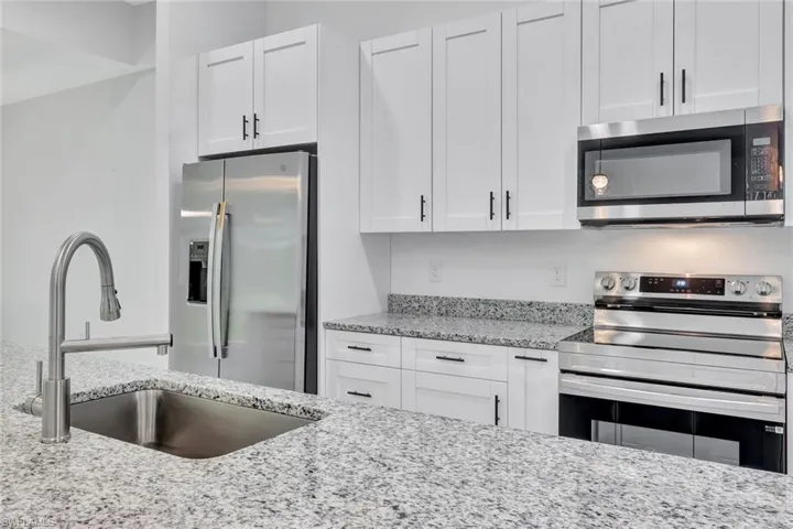 Kitchen with stainless steel appliances, white cabinetry, and light stone counters